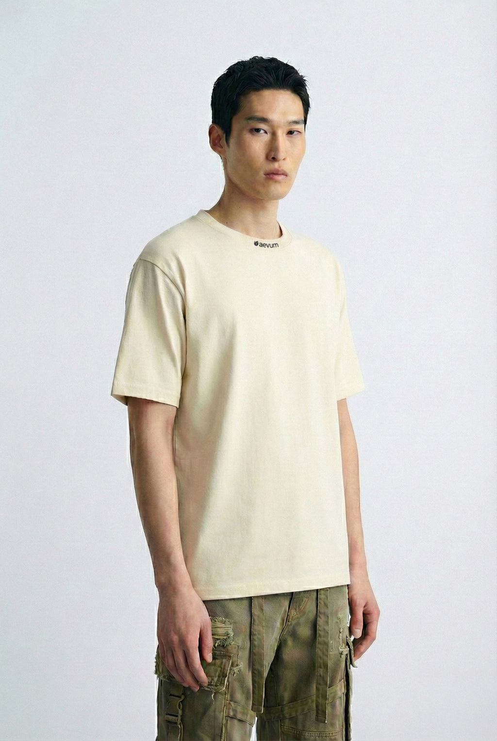 Person wearing a beige t-shirt and green cargo shorts on a white background