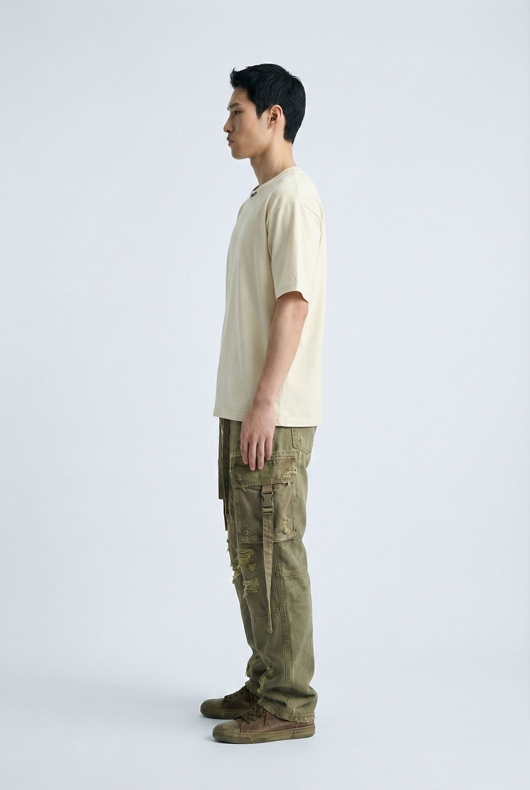 Person wearing a beige t-shirt and green cargo pants on a white background